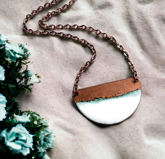 Necklace with a brown and white pendant on a textured surface with greenery.