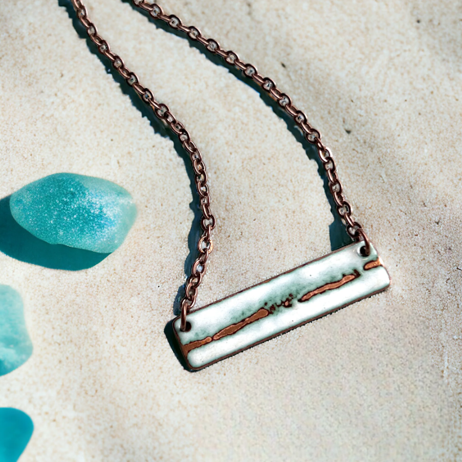 Necklace with a rectangular pendant on a sandy background with blue stones.