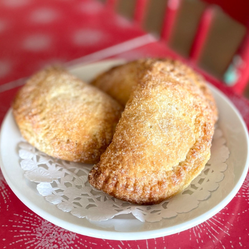 Two fried dough pastries on a white plate with a red tablecloth.