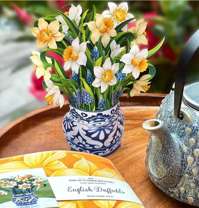 Vase with flowers on a wooden table next to a teapot and a book