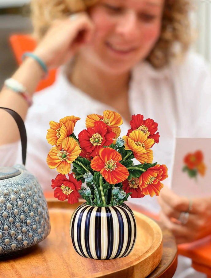 Striped vase with colorful flowers on a wooden table, blurred background of a person.