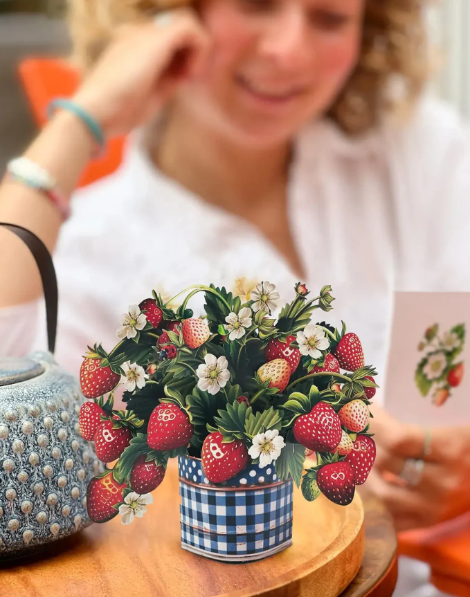 Decorative arrangement of strawberries in a pot on a table with a blurred person in the background.