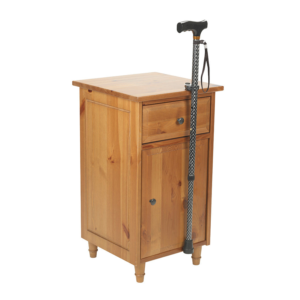 Wooden cabinet with a drawer and a walking cane leaning against it on a white background