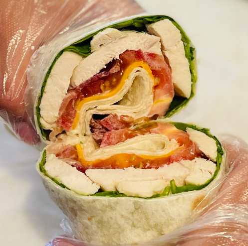 Half-eaten wrap with chicken, bacon, and cheese on a white surface