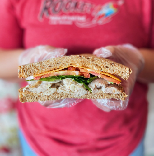 Person holding a sandwich cut in half with visible ingredients, wearing a red shirt with branding.