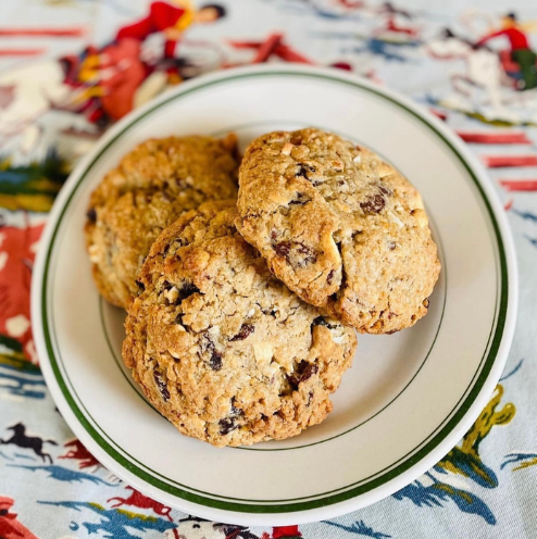 Three cookies on a white plate with green rim on a colorful fabric background