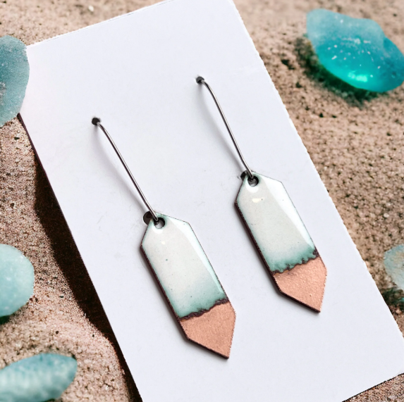 Pair of earrings with gradient design on a white card, sand background