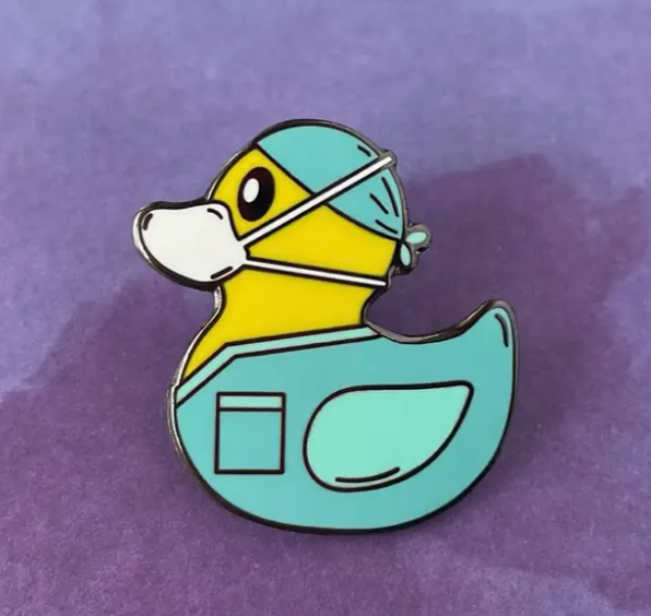Rubber duckie wearing a surgical mask and gown on a purple background