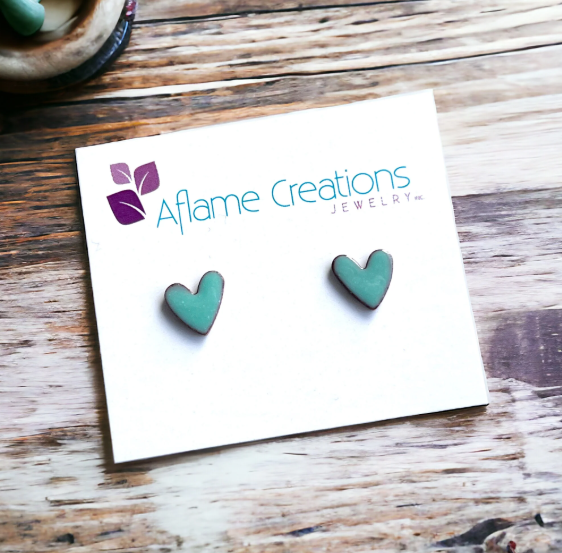 Teal heart-shaped earrings on a card with 'Aflame Creations Jewelry' logo on a wooden surface.