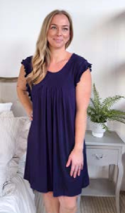 Woman wearing a navy blue dress standing in a room with a white wall and a plant.