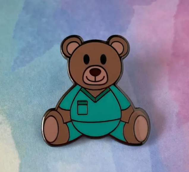Teddy bear pin with teal outfit on a watercolor background